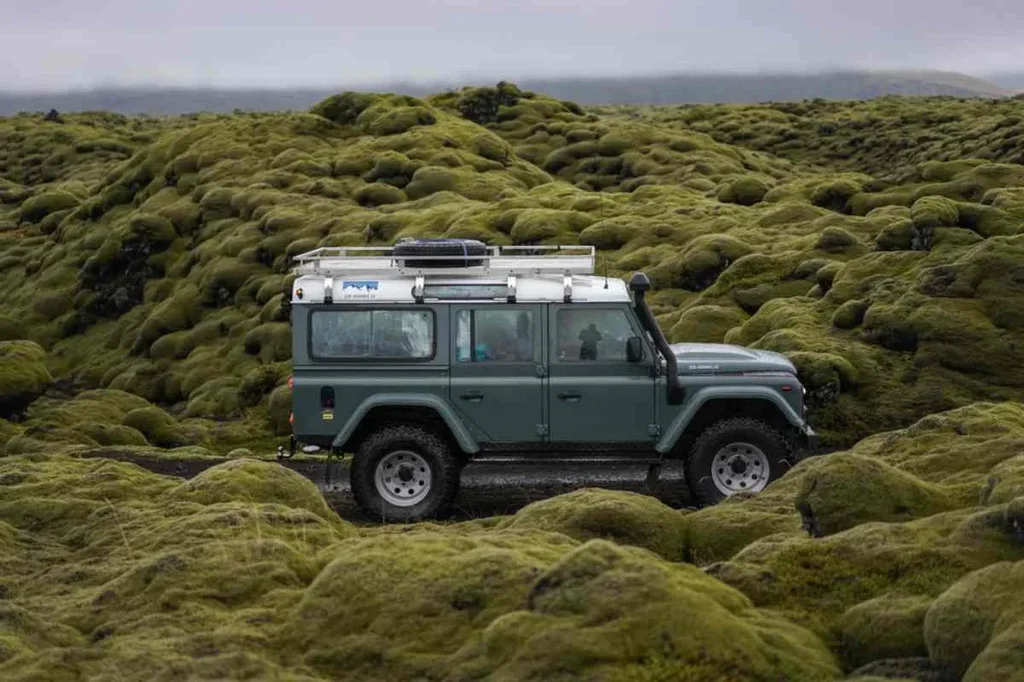 A green Land Rover driving through a lush moss-covered landscape in Iceland.