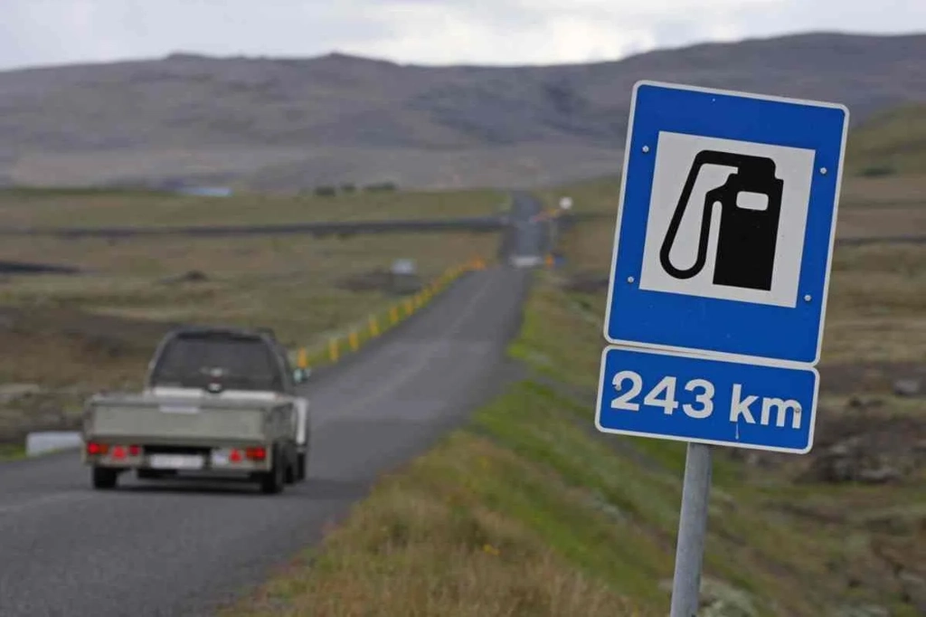 Road sign indicating the next gas station is 243 kilometers away, with a car driving on a remote road in Iceland.