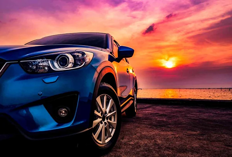 A blue SUV parked with a stunning sunset in the background, showcasing vibrant shades of pink, purple, and orange.