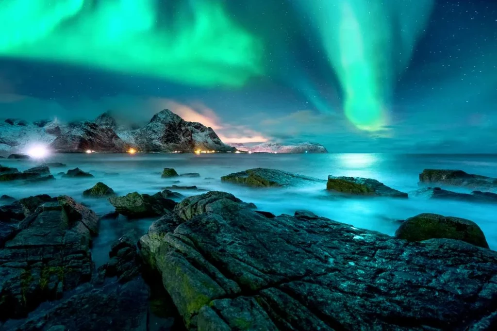 Stunning display of the Northern Lights over rocky coastal landscape in Iceland, with green auroras illuminating the night sky.