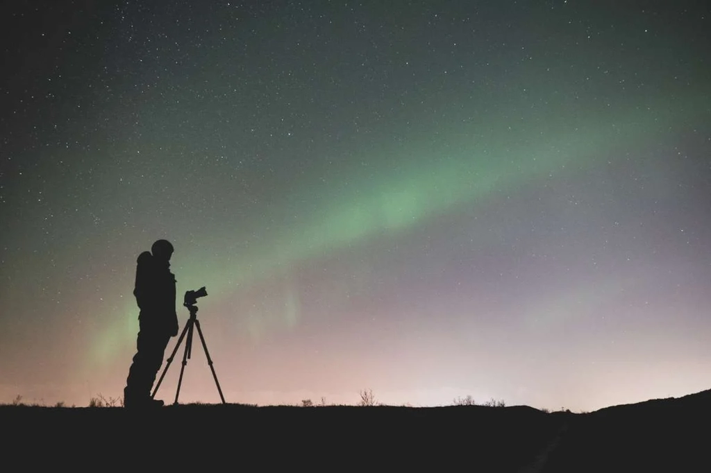 Silhouette of a photographer with a tripod capturing the Northern Lights in Iceland under a starry night sky.