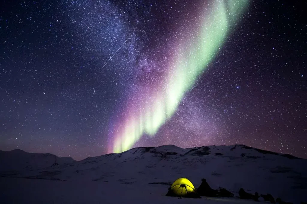 Tent illuminated under the Northern Lights in Iceland with a backdrop of a star-filled night sky.