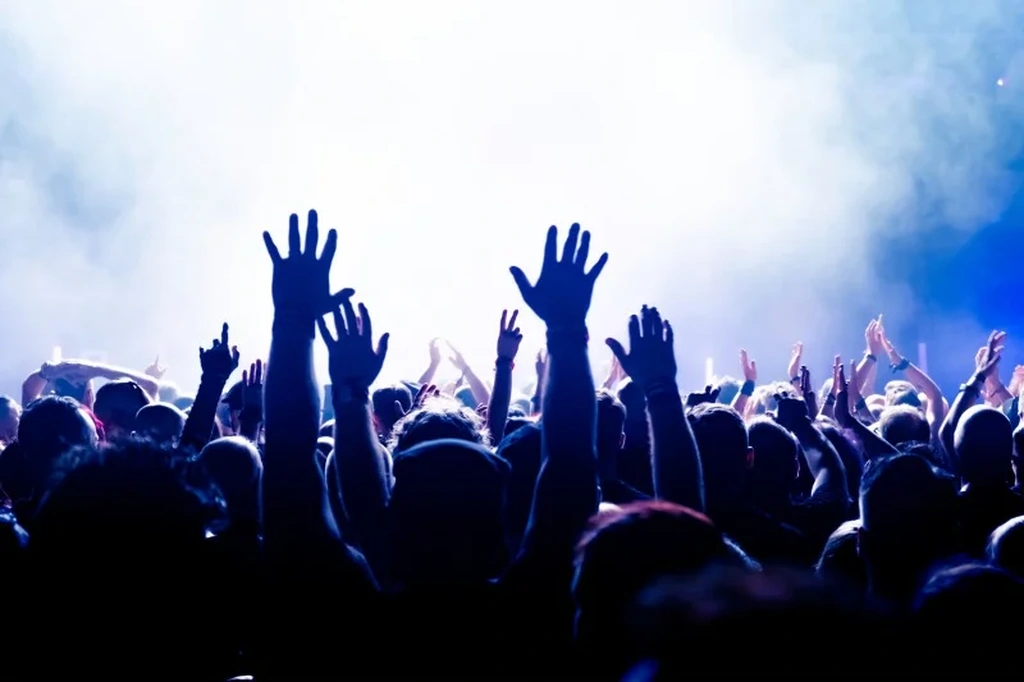 People raising their hands and enjoying a vibrant festival in Iceland, illuminated by bright stage lights and surrounded by a cloud of mist.