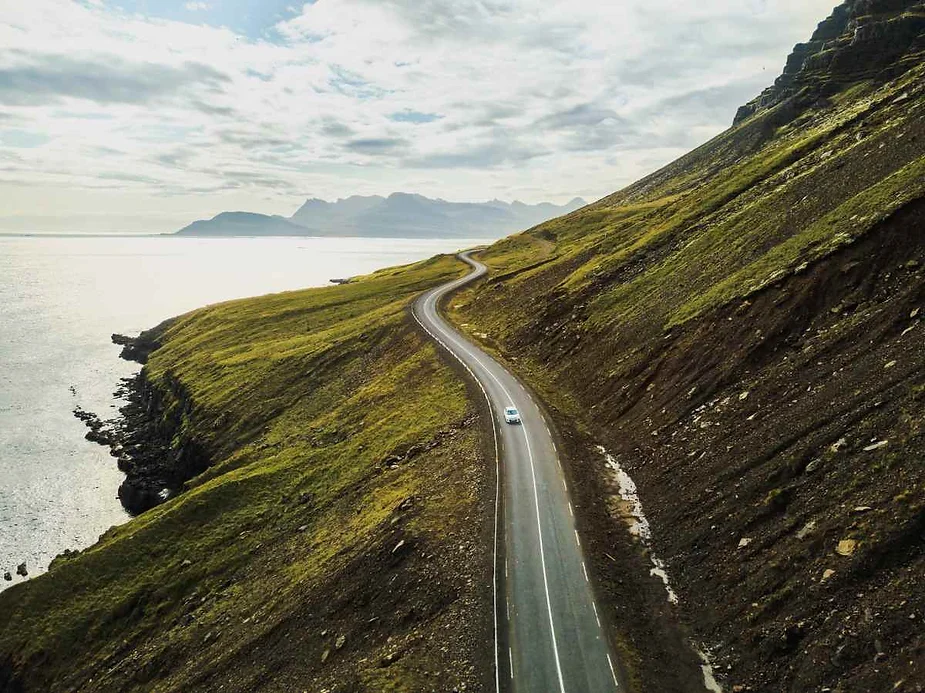 A scenic drive along the winding coastal road in Iceland, showcasing the stunning landscape with a backdrop of mountains and the ocean.