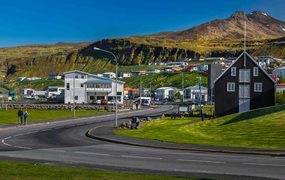 Charming Icelandic village nestled in a valley with colorful houses, green hills, and clear blue skies, epitomizing the serene beauty of Icelandic rural life.