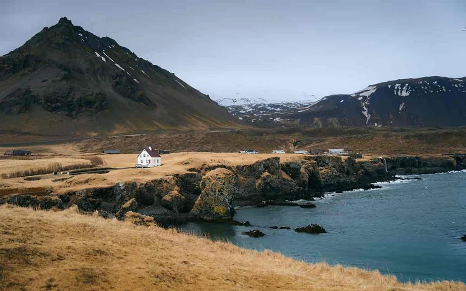 A picturesque scene of a solitary white house on the rugged coast of Iceland, framed by towering mountains and a serene sea.