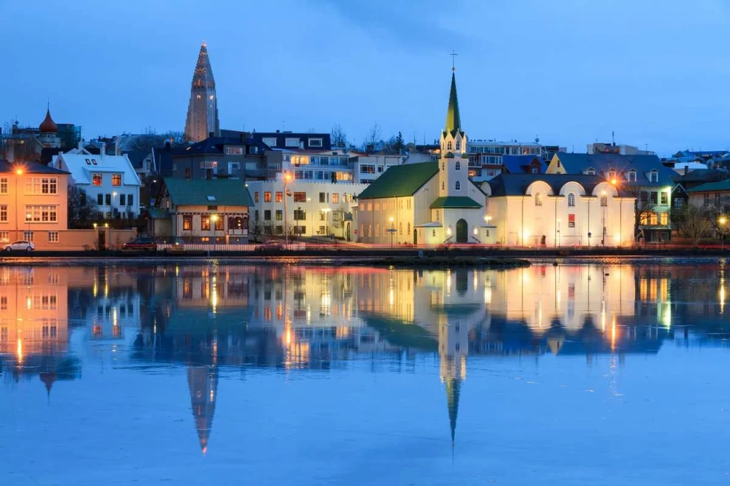 Reykjavik cityscape at twilight with illuminated buildings and their reflections in the calm water.