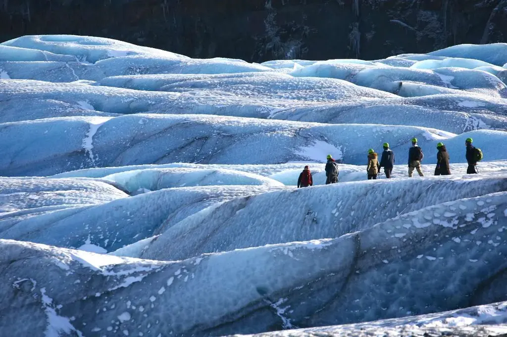 Group of hikers exploring the blue ice formations of a glacier in Iceland, wearing helmets and winter gear.