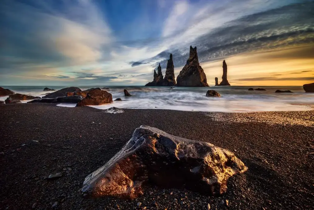 Stunning view of Reynisdrangar sea stacks at sunset, with black sand beach and dramatic skies in Iceland.