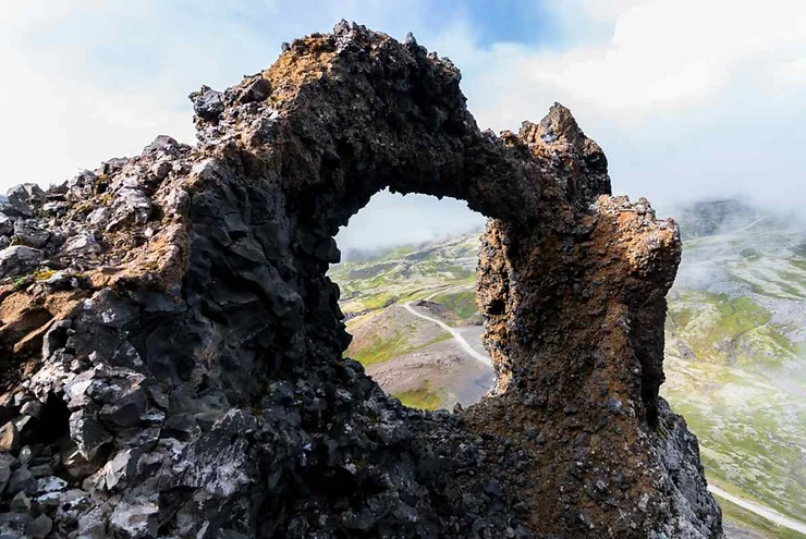 A striking rock formation at Sönghellir Cave in Iceland, featuring a natural archway with a view of the surrounding landscape and a misty sky in the background.