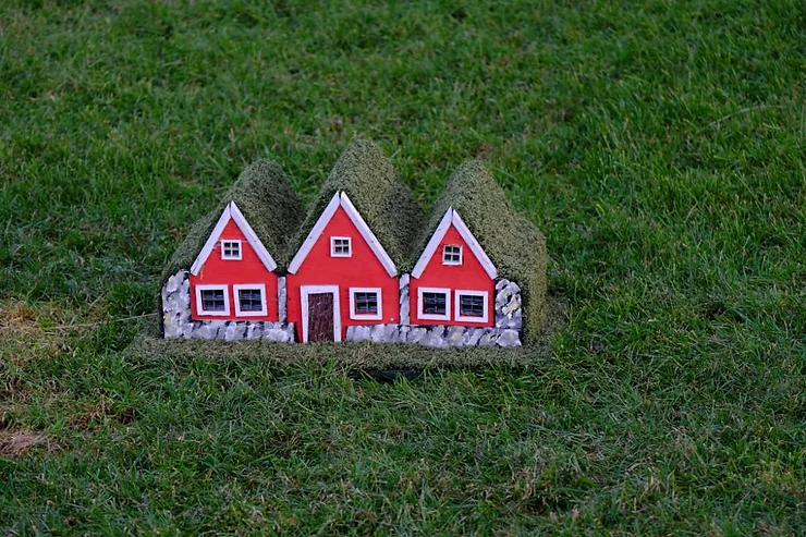 A charming set of small red elf houses with white trim and grass-covered roofs, set on a green grassy landscape in Iceland.