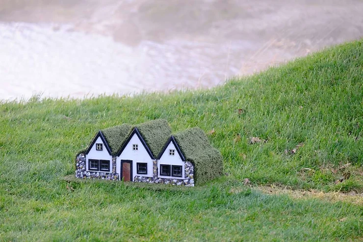 A charming miniature elf house nestled in the green grass of Iceland, showcasing the whimsical and enchanting folklore of the region.