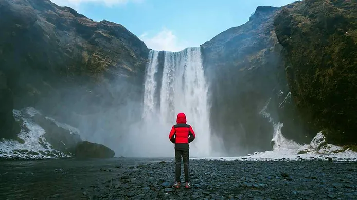 tourist standing in front of skogafoss waterfall