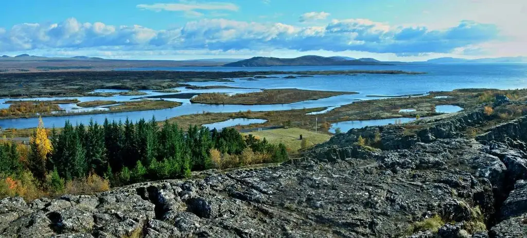 Signpost pointing to Thingvellir in Iceland, standing in a snow-covered landscape with the sun rising or setting in the background.