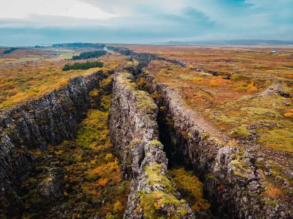 A hiker walking along a wooden path between towering rock formations at Thingvellir National Park in Iceland, under a clear blue sky.