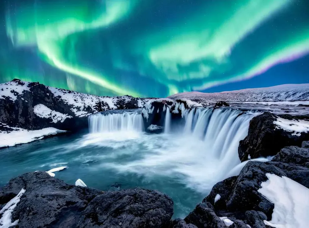 Goðafoss waterfall in Iceland under the vibrant Northern Lights, with snow-covered rocks and flowing water creating a magical winter scene