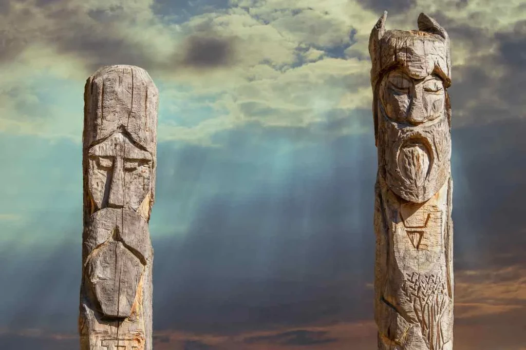 Two wooden Viking totems carved with ancient faces, set against a dramatic sky with rays of sunlight breaking through the clouds