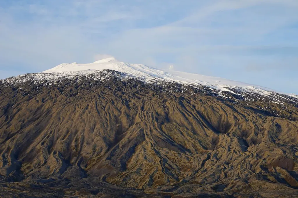 Snow-covered peak of Snæfellsjökull volcano in Iceland, with rugged, eroded slopes leading up to the summit under a clear sky