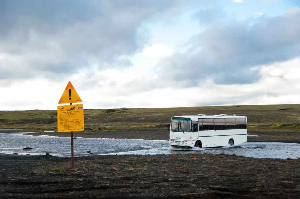 Two buses parked under the mesmerizing display of the Northern Lights in Iceland, with vibrant green auroras lighting up the night sky.