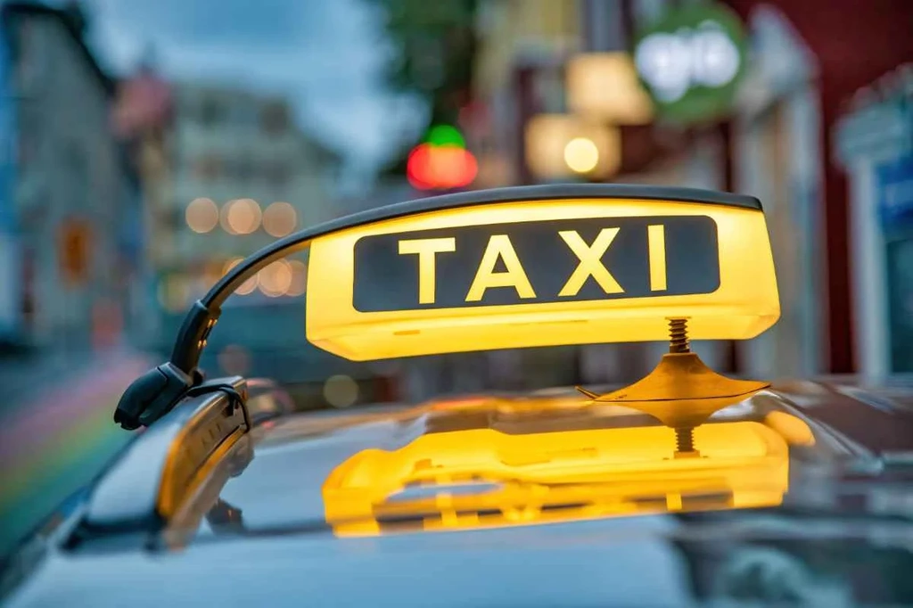 Close-up of an illuminated yellow taxi sign on a car roof in Iceland, with blurred city lights in the background