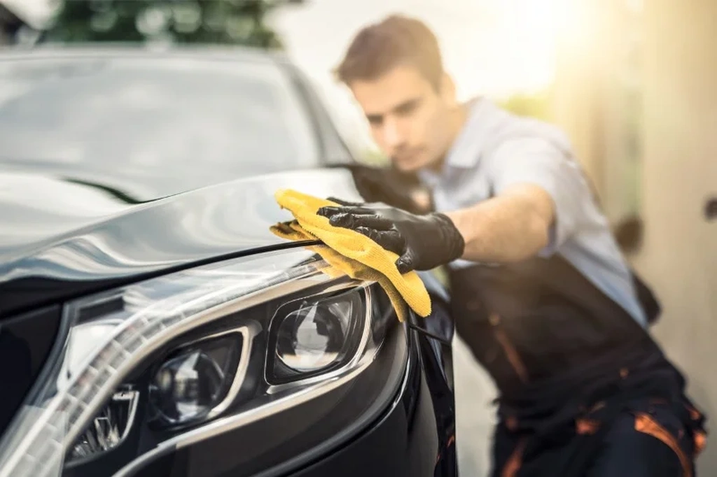 Professional auto detailer polishing the headlight of a shiny black European car, ensuring a pristine finish and enhancing its luxury appeal.