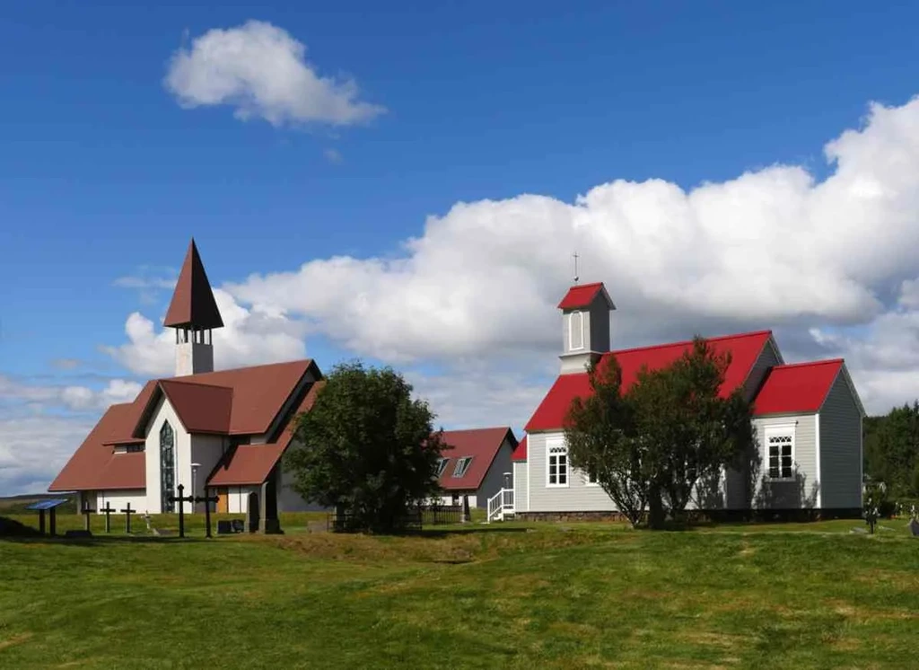 Historic churches in Reykholt, Iceland, featuring traditional red roofs and a serene landscape under a bright blue sky.