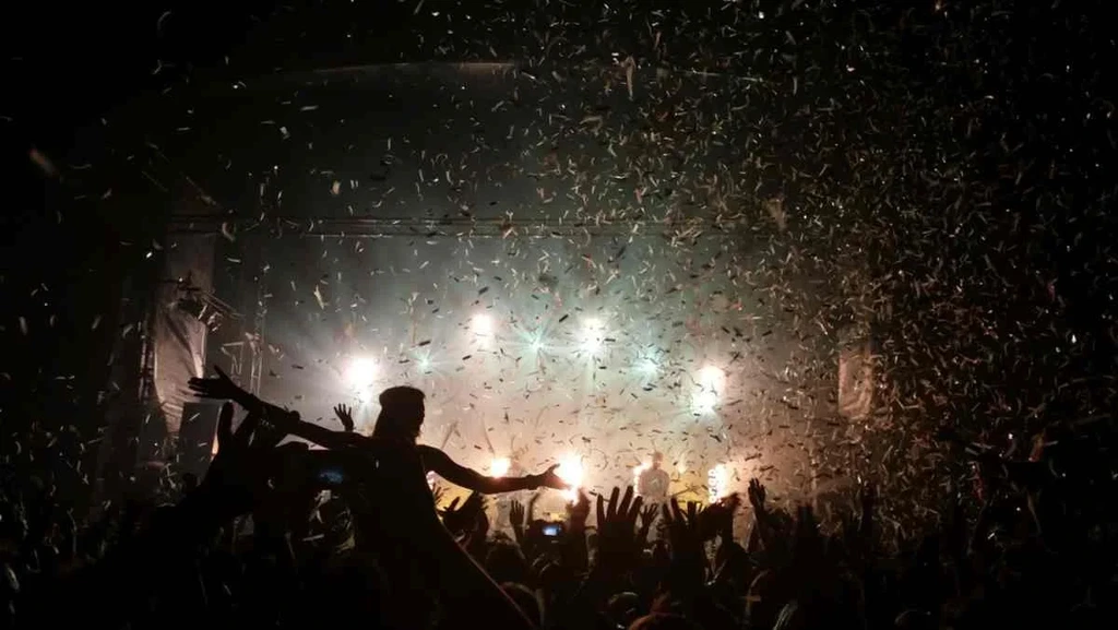 Concert crowd celebrating under a shower of confetti with bright stage lights illuminating the scene at a lively festival in Iceland.