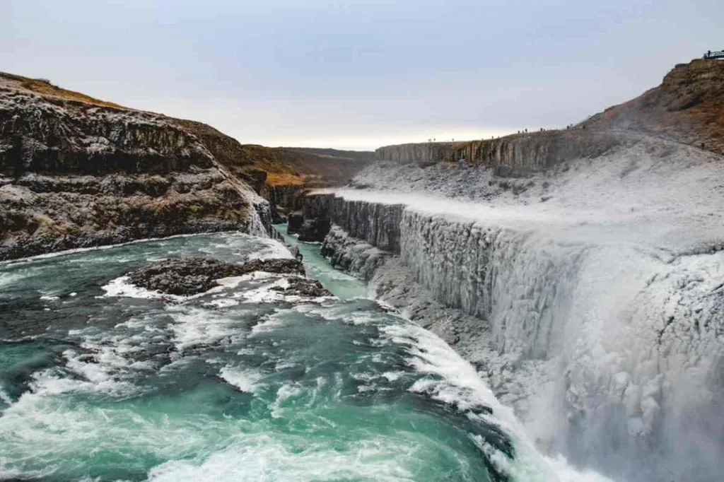 Gullfoss waterfall in Iceland during winter, with powerful cascading water partially frozen, surrounded by rocky cliffs and icy mist.