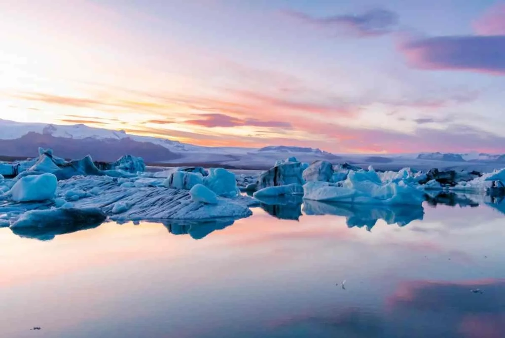 Jökulsárlón Glacier Lagoon in Iceland at sunset, with icebergs floating on calm, reflective waters, under a pastel-colored sky.