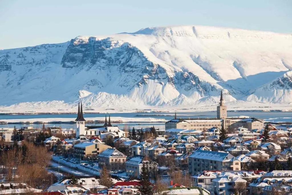 Winter panorama of Reykjavik, Iceland, with snow-covered rooftops and iconic church spires, set against a backdrop of majestic snow-capped mountains.