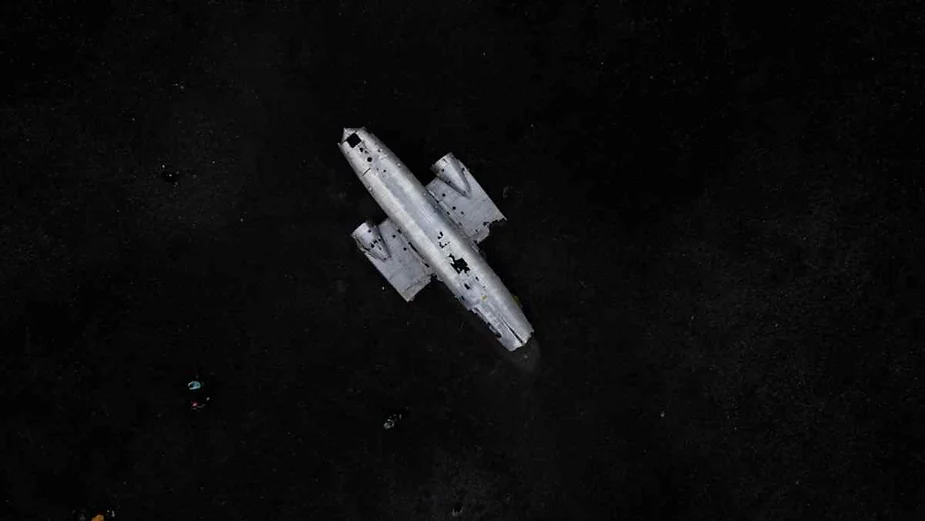 Aerial view of an abandoned plane wreck on a stark black sand beach in Iceland.