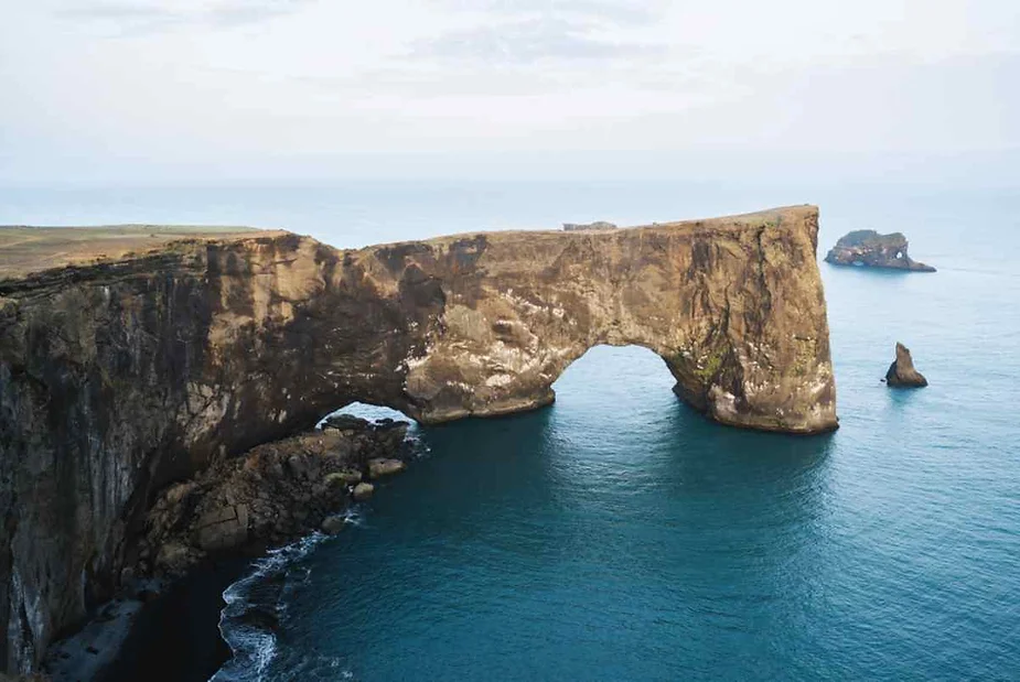 Stunning aerial view of the Dyrhólaey rock arch on the southern coast of Iceland, surrounded by the blue waters of the Atlantic Ocean.