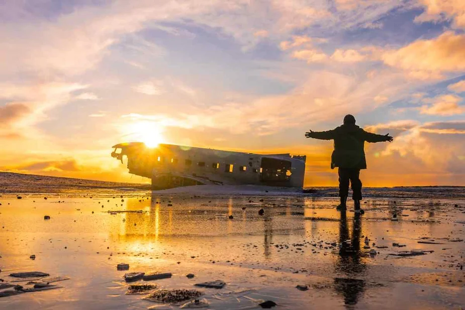 Man embracing the stunning sunrise at the Solheimasandur plane wreck in Iceland, with the abandoned aircraft silhouetted against the colorful sky.