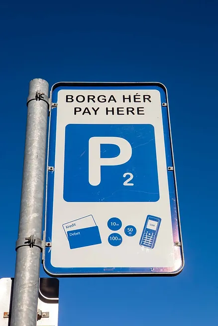 Parking payment sign with instructions in both Icelandic ('Borga Hér') and English ('Pay Here') against a clear blue sky.