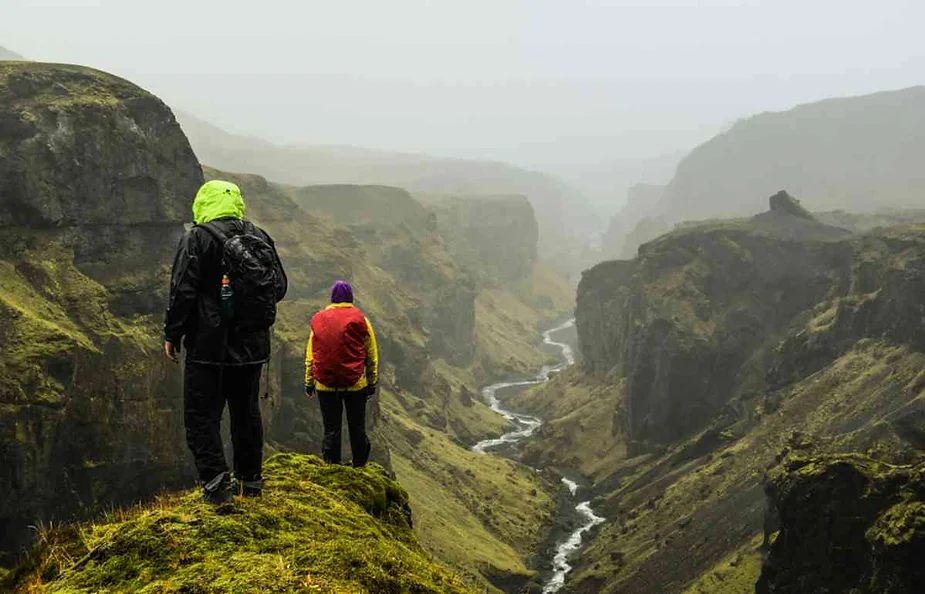 Hikers standing on a foggy cliff overlooking a deep canyon with a river winding through it.