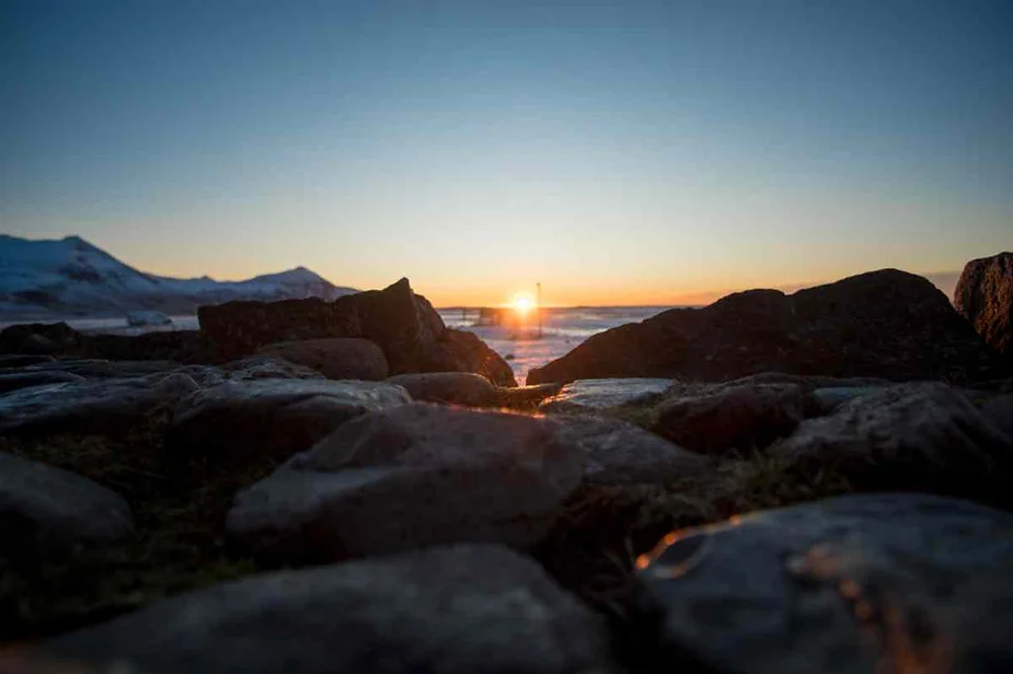 Sunset view with rocky foreground and snow-covered mountains in the background.