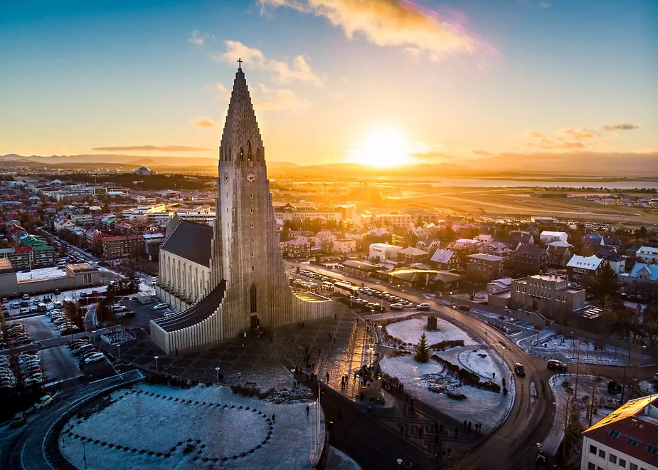 Hallgrimskirkja Church in Reykjavik, Iceland, during a vibrant sunrise, overlooking the city with snow-covered rooftops and distant mountains.