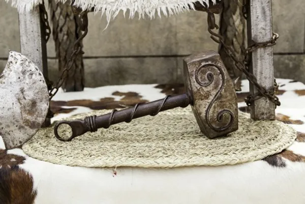 Viking hammer with ornate designs resting on a woven mat with fur and chain decorations in the background.