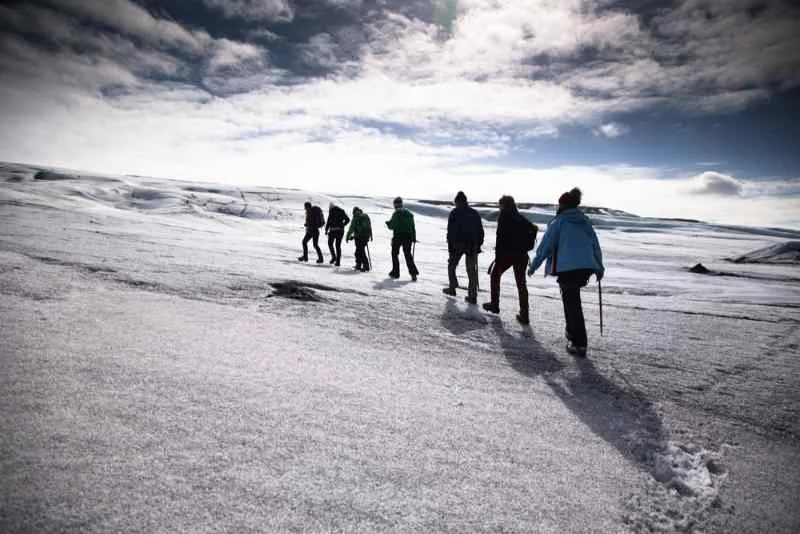 Group of people hiking across a snowy landscape under a partly cloudy sky.