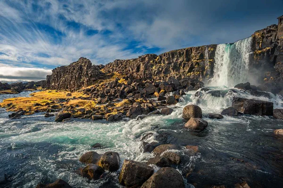 Scenic view of Öxarárfoss waterfall cascading over rocky cliffs in Thingvellir National Park, Iceland, surrounded by rugged terrain and vibrant autumn colors.