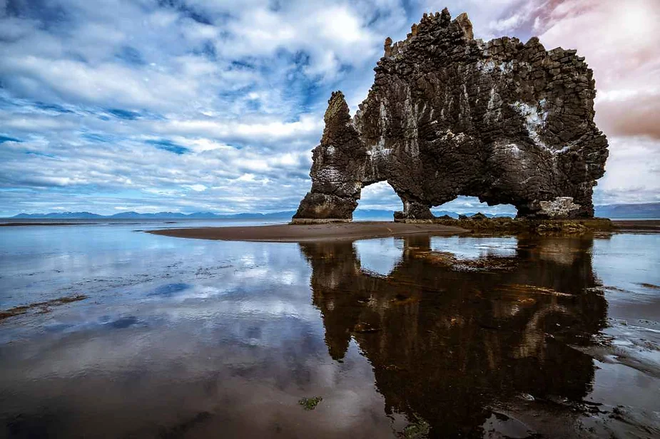 Hvítserkur, a striking rock formation resembling a dragon or dinosaur drinking from the sea, reflected in the calm waters at low tide in Iceland.