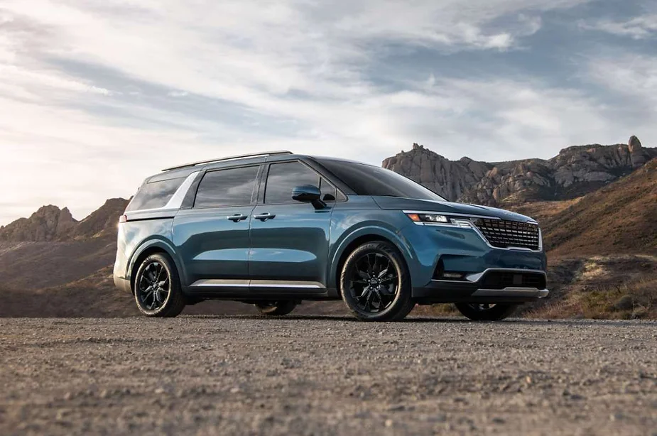 A stylish blue SUV parked on a gravel road with rugged mountain terrain in the background, showcasing its sleek design and modern features under a partly cloudy sky.