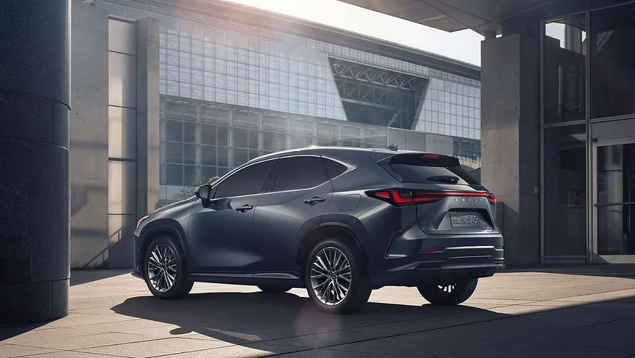 A sleek Lexus NX SUV parked in a modern urban environment, featuring sharp lines, tinted windows, and stylish alloy wheels against the backdrop of contemporary architecture.