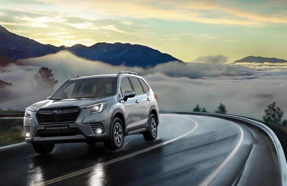 A Subaru Forester SUV navigating a winding mountain road at dawn, with mist-covered valleys and distant peaks creating a serene and adventurous backdrop.