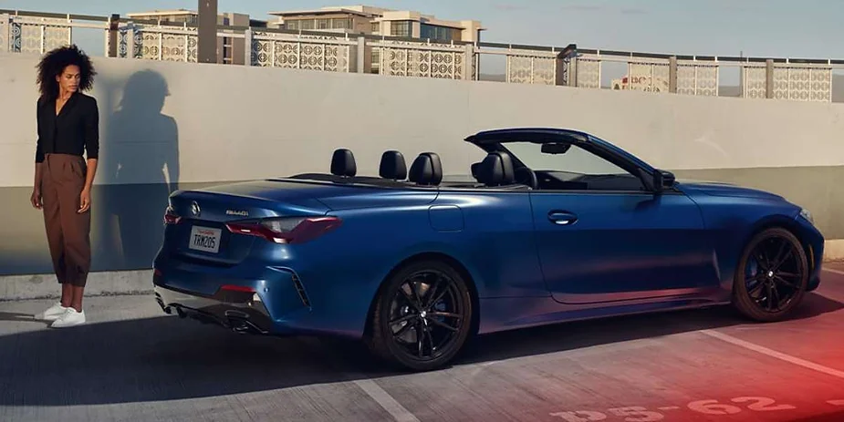 A sleek blue BMW convertible parked in an urban rooftop setting, with a stylish woman standing nearby, exuding elegance and modern luxury.