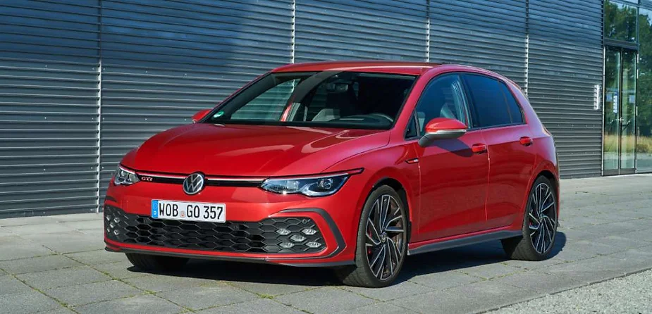 A bright red Volkswagen Golf GTI parked in front of a modern building, showcasing its sporty design, aggressive front grille, and sleek alloy wheels.