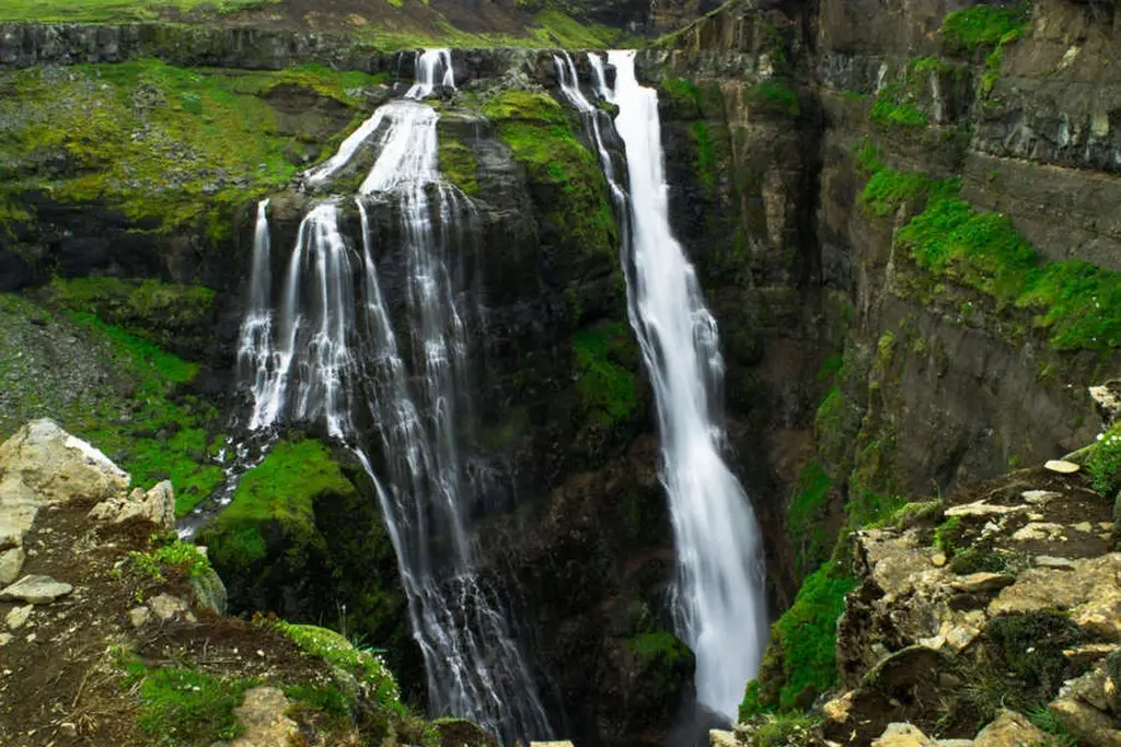 Majestic view of Glymur Waterfall in Iceland, cascading down a steep cliff surrounded by lush green vegetation and rugged rock formations.