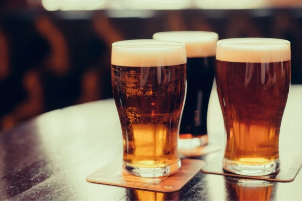 A flight of four Icelandic craft beers on a wooden tray with a bowl of pretzels and nuts in the background, showcasing the variety of brews available in Iceland.