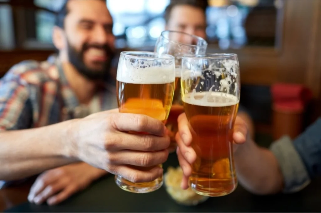 Three friends clinking their glasses of Icelandic beer in a cheerful pub setting, capturing the social culture of drinking in Iceland.