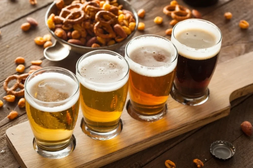 A flight of four Icelandic craft beers on a wooden tray with a bowl of pretzels and nuts in the background, showcasing the variety of brews available in Iceland.